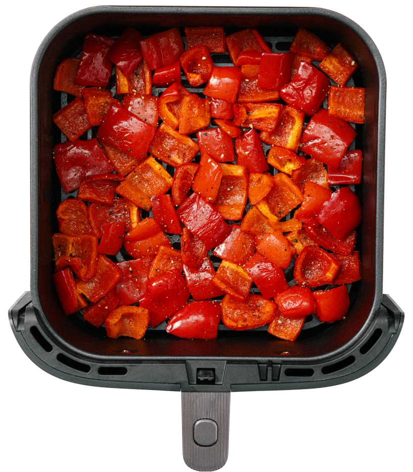 Chopped red bell peppers seasoned and placed in a black air fryer basket.